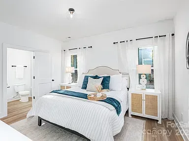 Bright white bedroom with a neatly made bed, teal accents, and wicker nightstands near two windows.