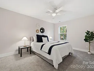 Bright bedroom with a white bed, bedside lamp, window, carpet, and potted plant