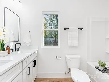 Bright white bathroom with vanity sink, toilet, window, towel rack, and potted plant.