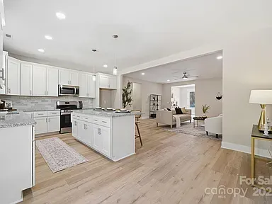 Bright, open-concept kitchen and living room with white cabinets, gray island, and light wood floors.