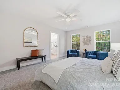 Bright bedroom with a bed, blue chairs, mirror bench, and two windows