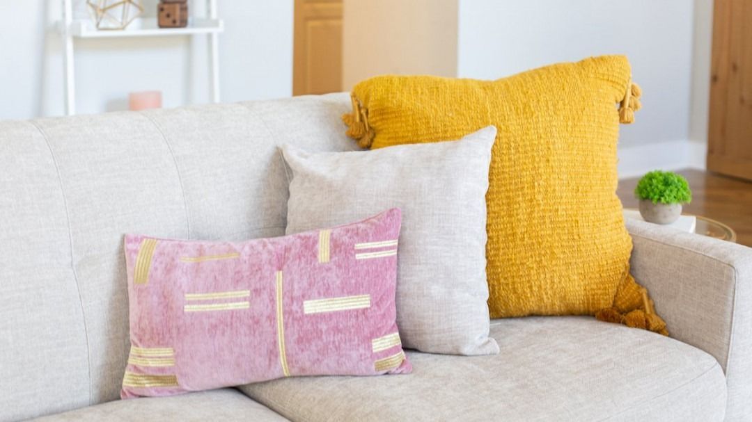 Light beige sofa with white, pink, and yellow textured throw pillows in a bright living room