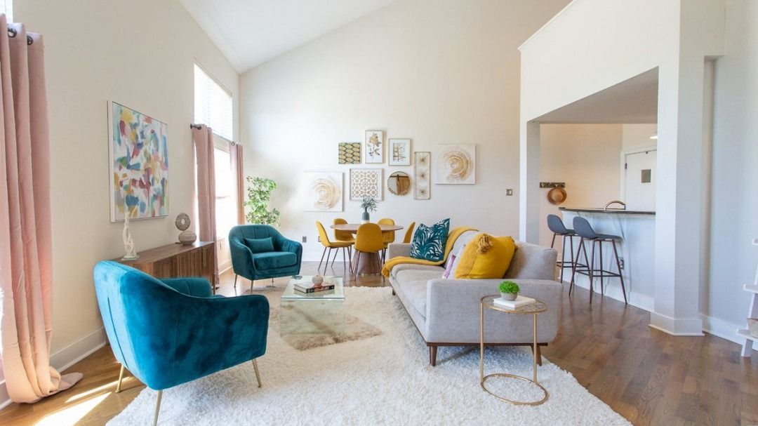 Bright living room with teal and yellow chairs, white sofa, wood floors, and colorful wall art