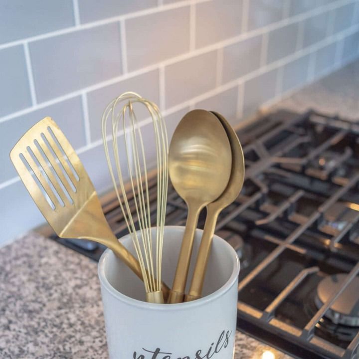 Gold kitchen utensils in a ceramic holder on a countertop beside a gas stove.