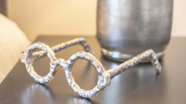 Wire-frame eyeglasses on a dark table with a blurred metal cup in the background