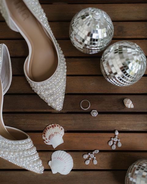 Sparkly white heels and shell jewelry arranged on a dark wooden floor with silver disco balls