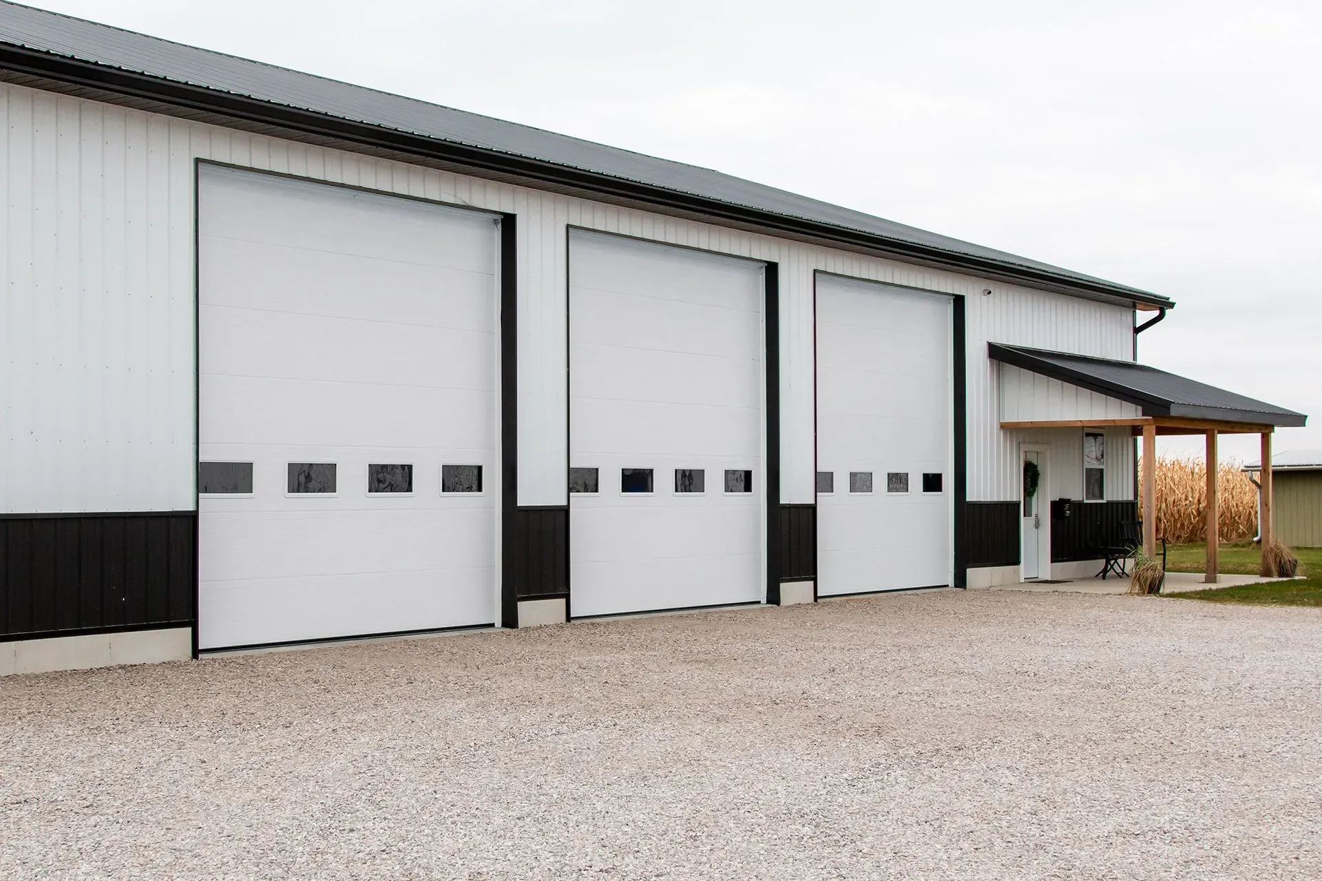 .Large Garage Door Commercial with three garage doors and a small covered entryway. Gravel driveway.