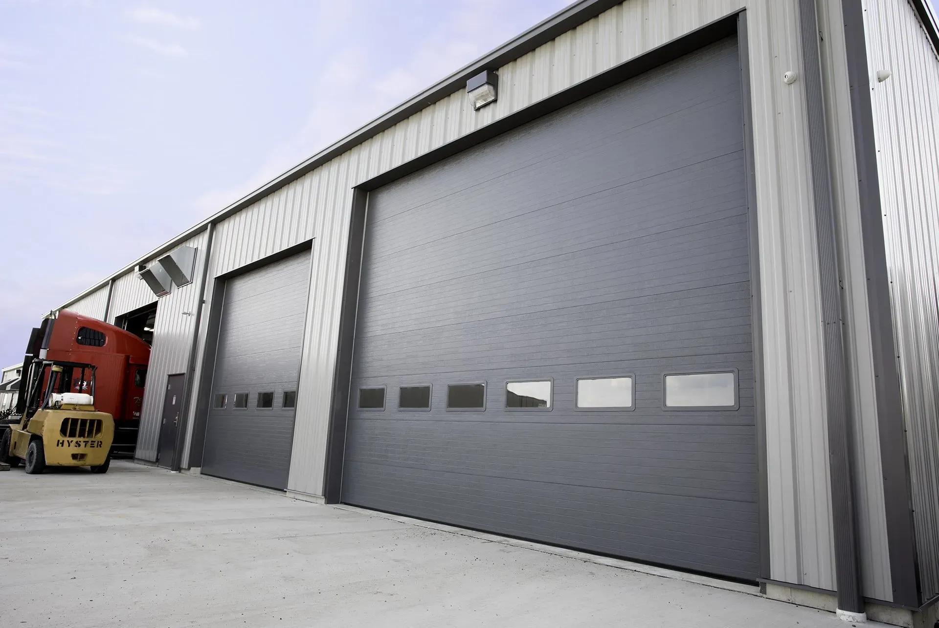 .Large Garage Door CommercialGray industrial building with closed overhead doors; a truck is parked inside one.