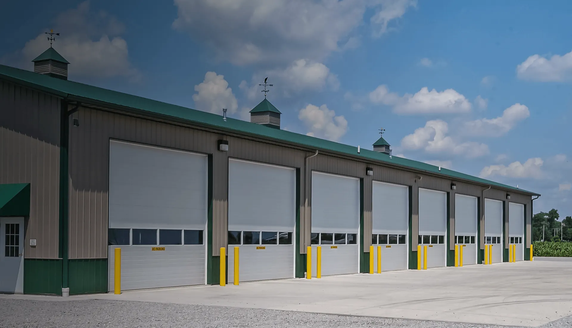 Large industrial building with multiple bay doors, green roof, and clear blue sky.