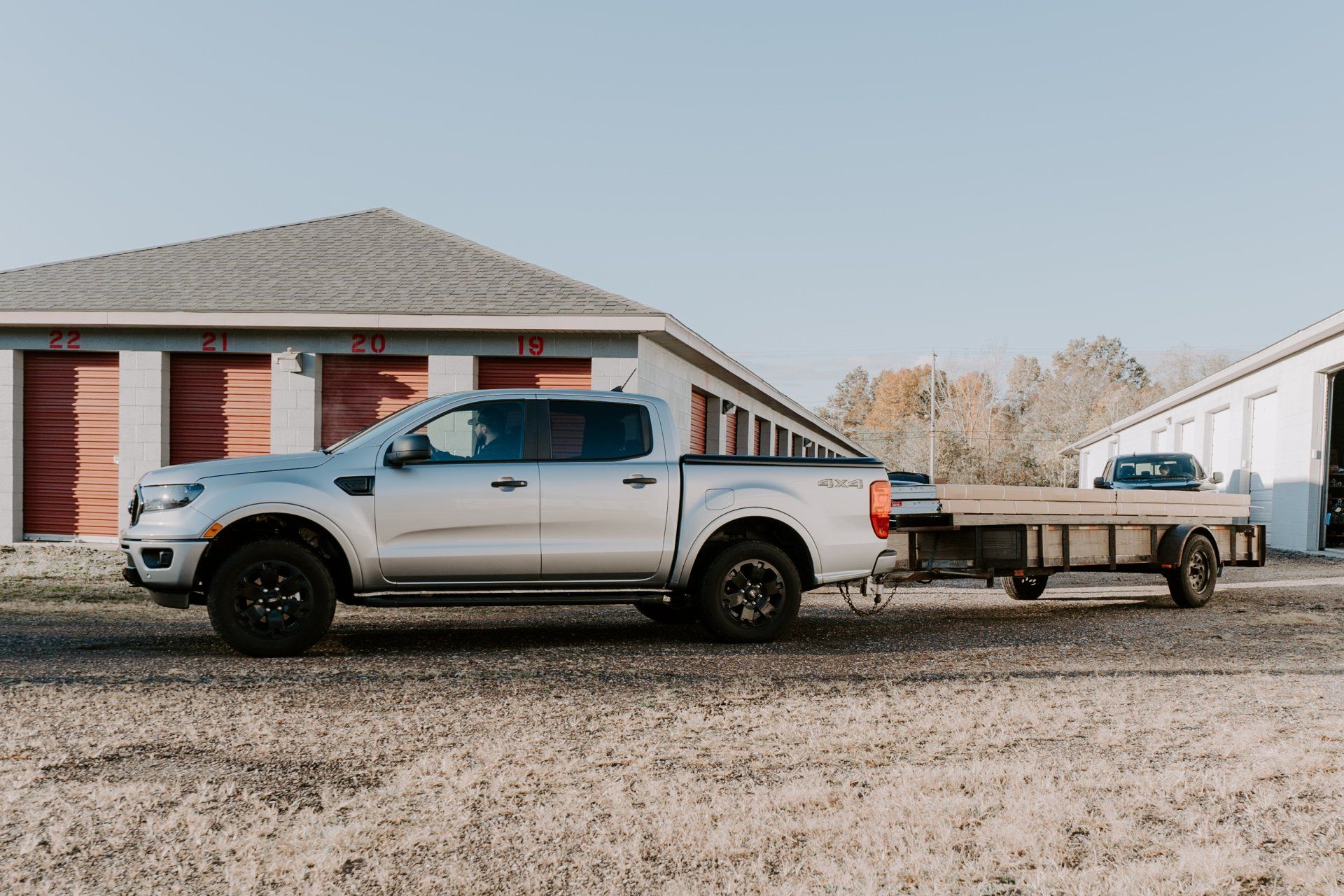 Silver pickup truck towing a trailer in front of storage units.