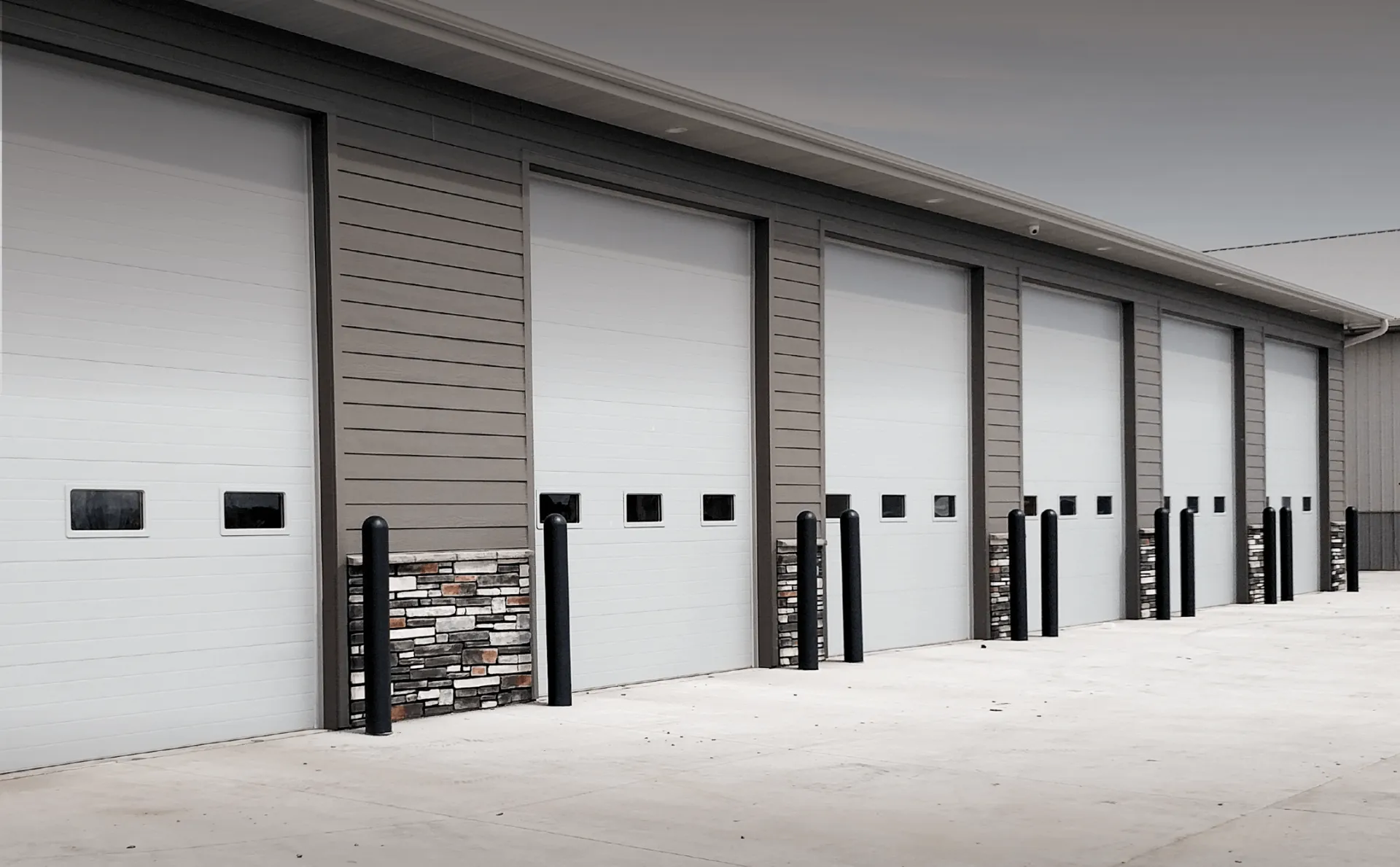 Exterior view of a building with multiple white loading dock doors and metal framing.