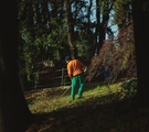 Person in orange shirt and green pants walking in a wooded area behind a fence.