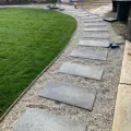 Hands rolling out a strip of grass sod on a lawn outdoors.