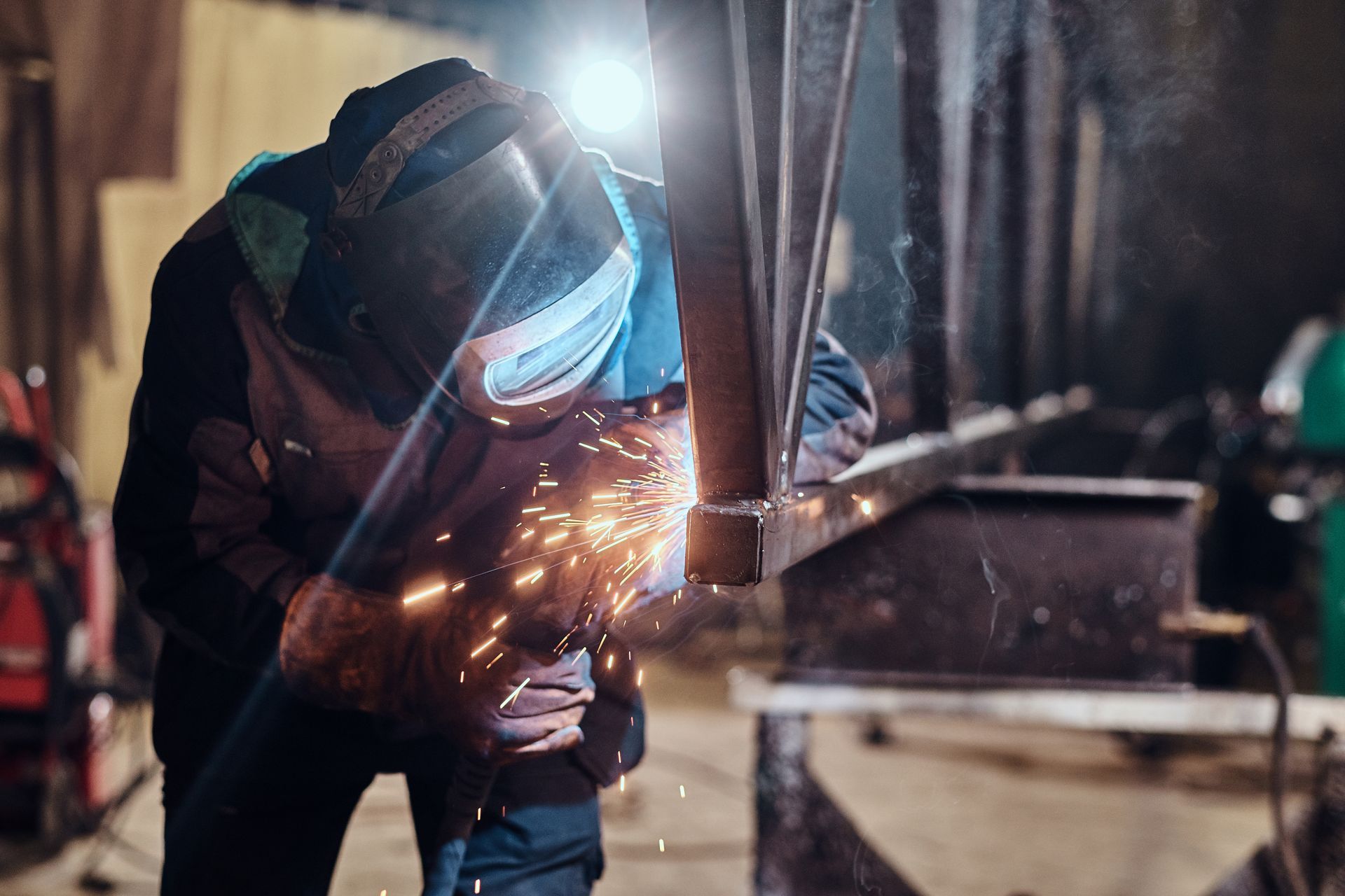 Welder in protective gear grinding metal beam, sparks flying in workshop.