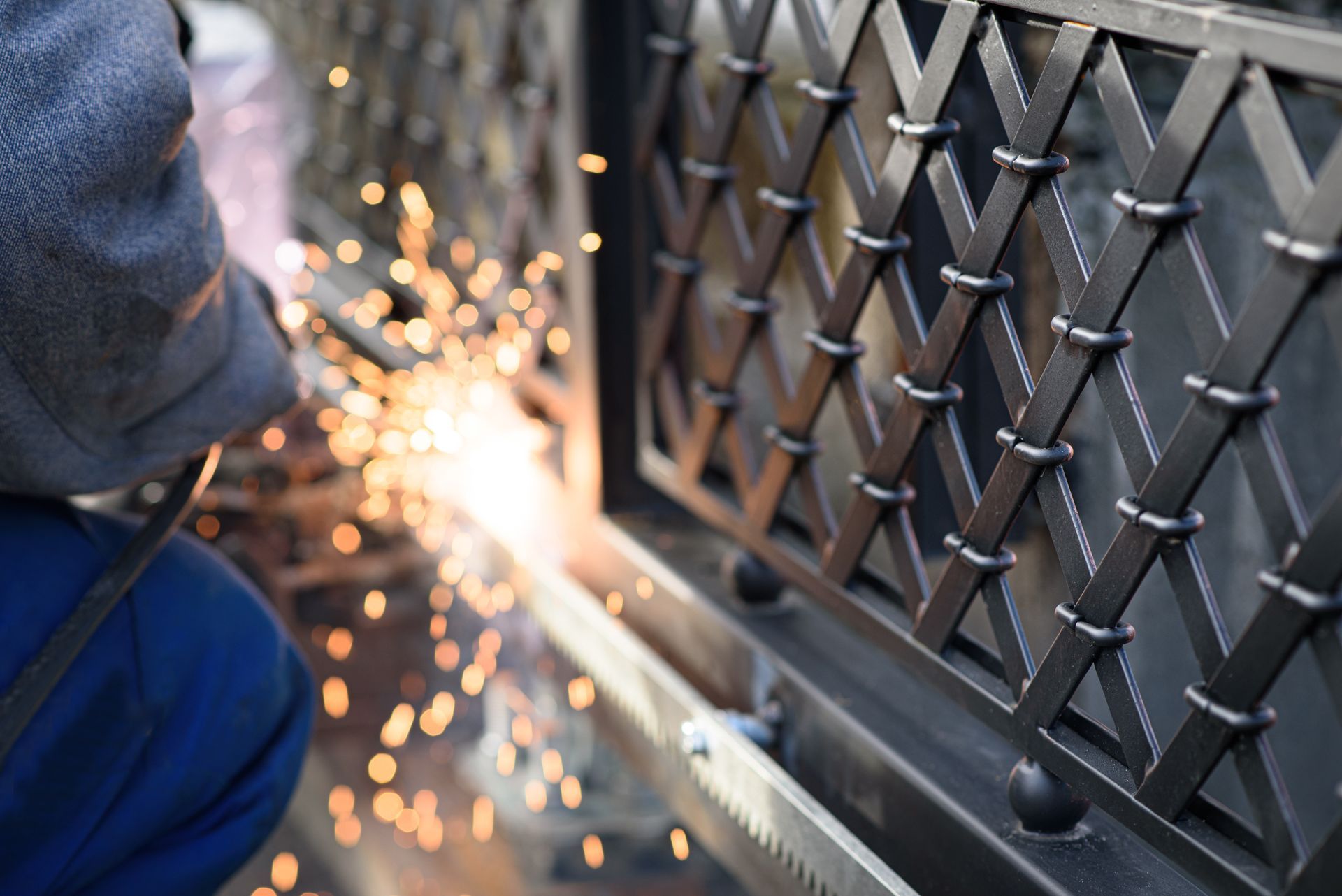 Worker welding metal gate, sparks flying during fabrication process.