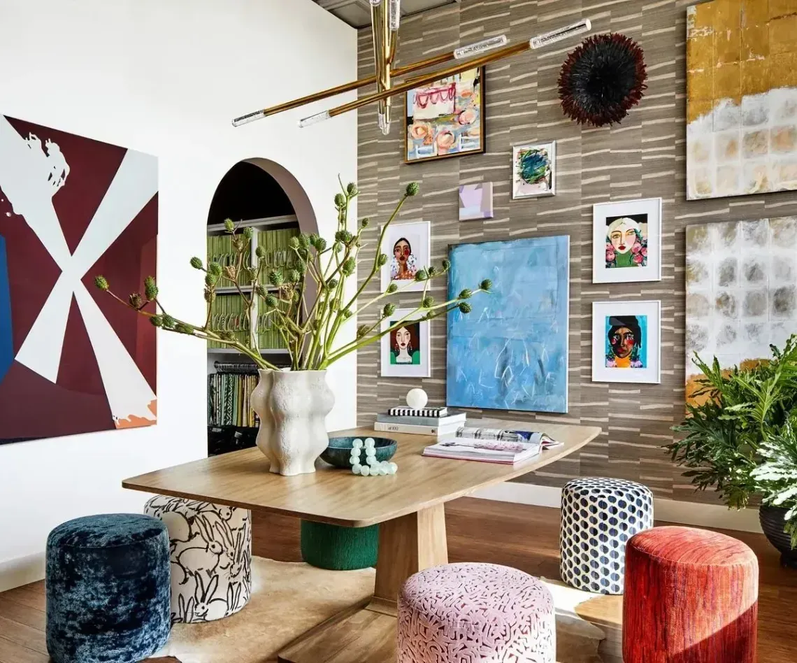 A dining room with colorful art on the walls, a wooden table, and patterned stools.