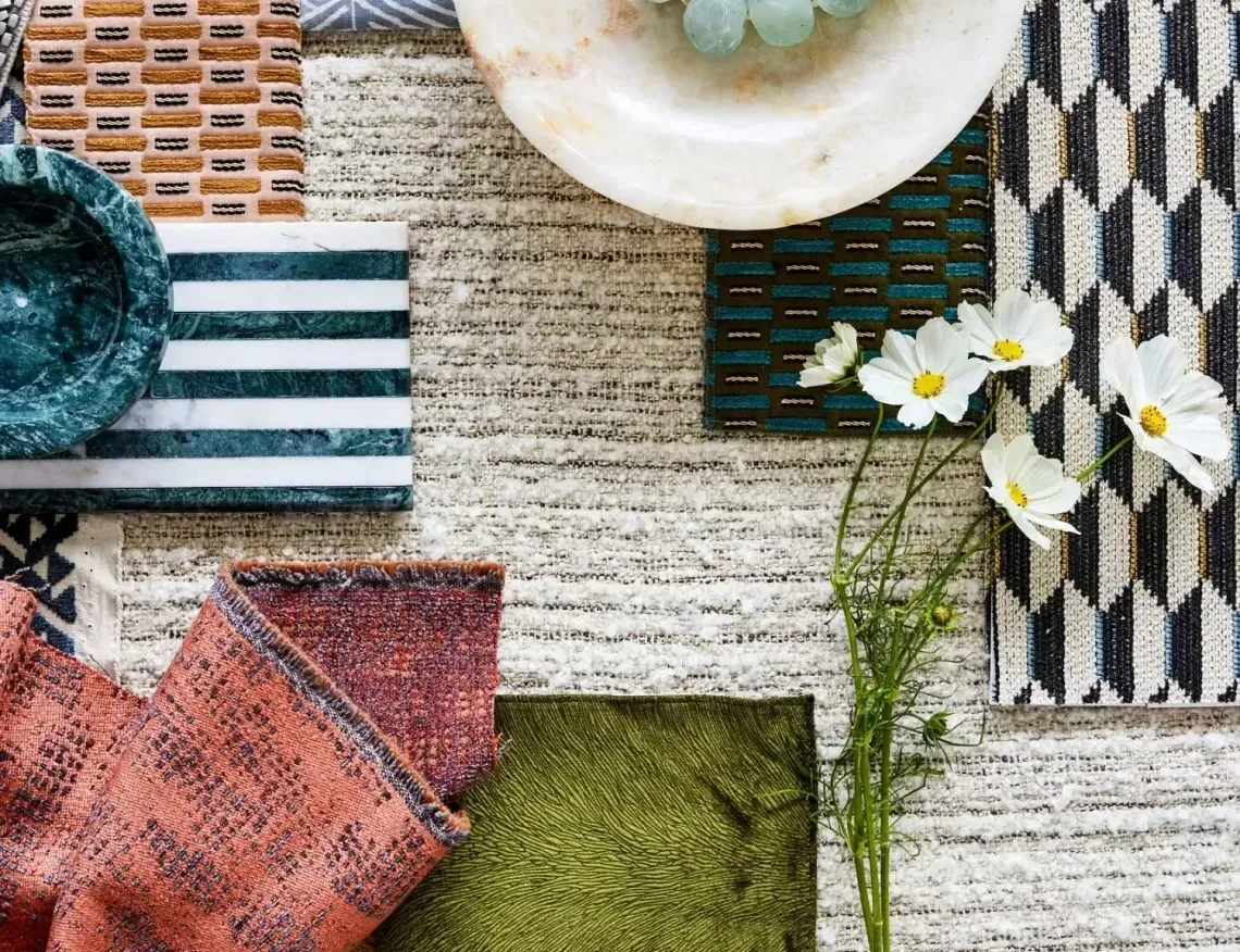 Assorted textiles, dishware, and flowers arranged on textured white surface.  Various colors include green, blue, and coral.