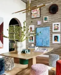 Room with a wooden table, colorful stools, and art-filled wall. Includes a green plant and an archway with books.