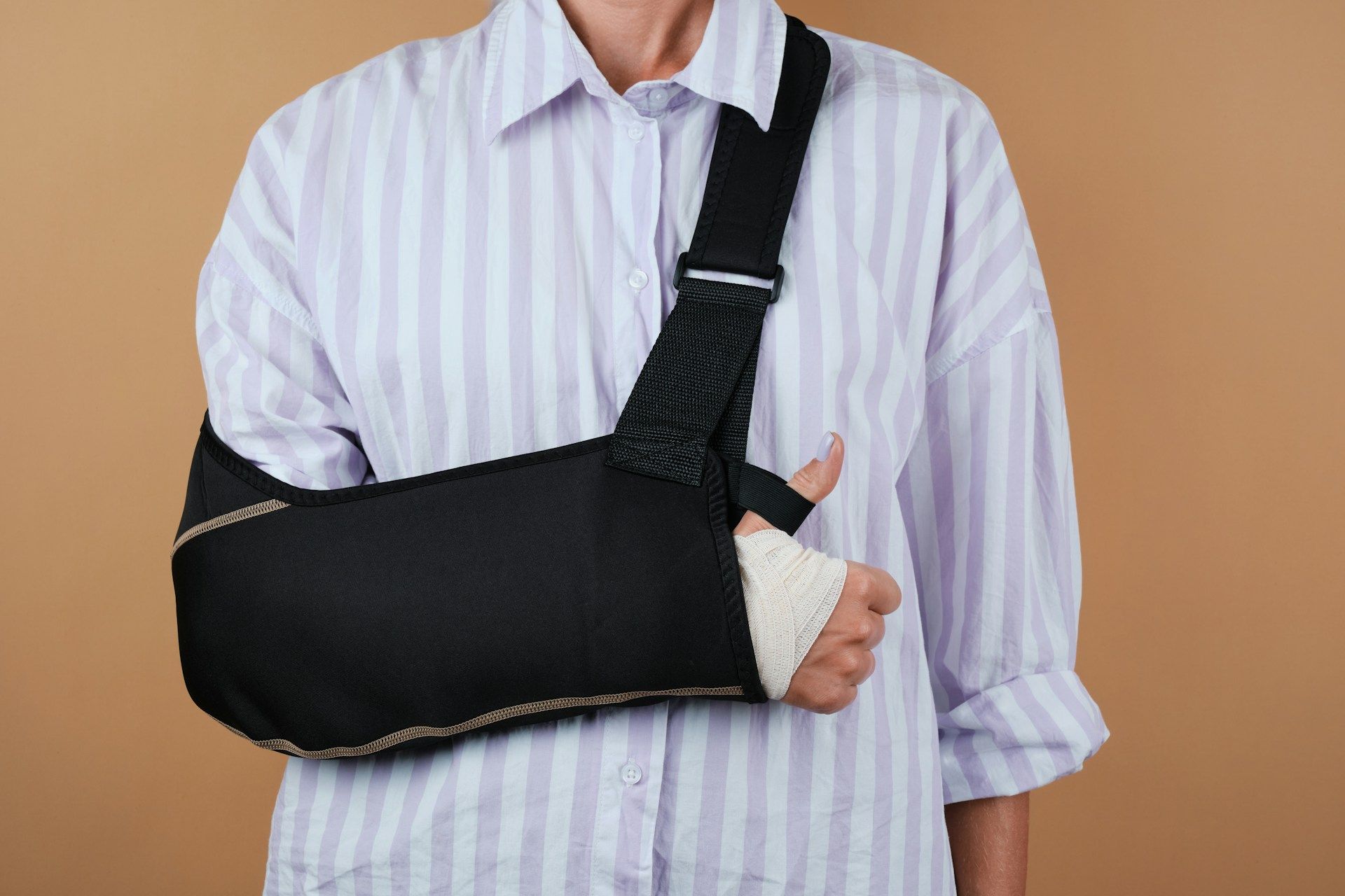 Person wearing a black arm sling over a striped shirt against a plain background
