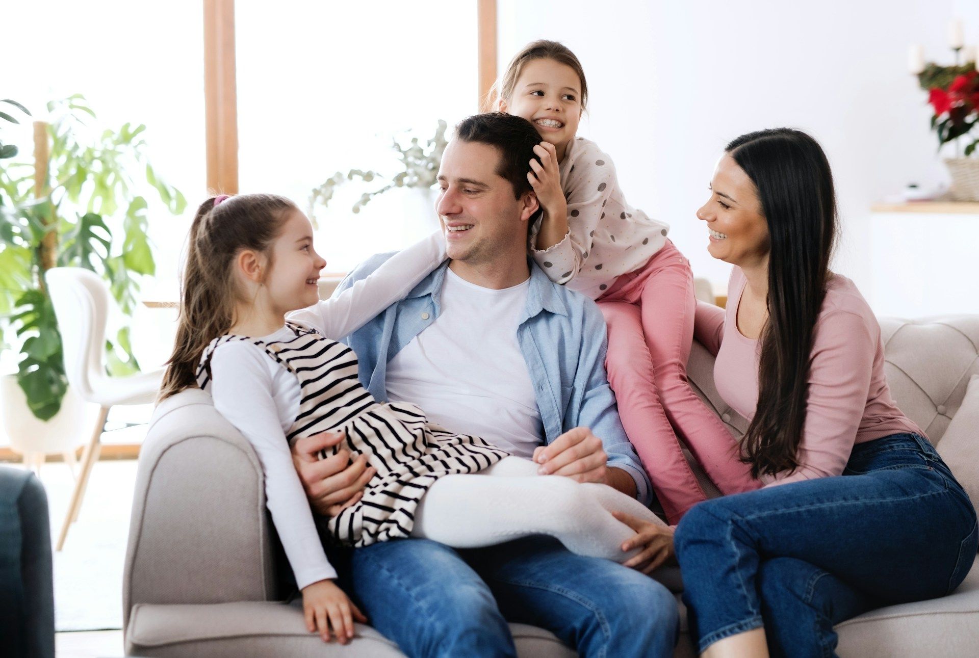 Family of four sitting together on a couch, smiling in a bright living room.