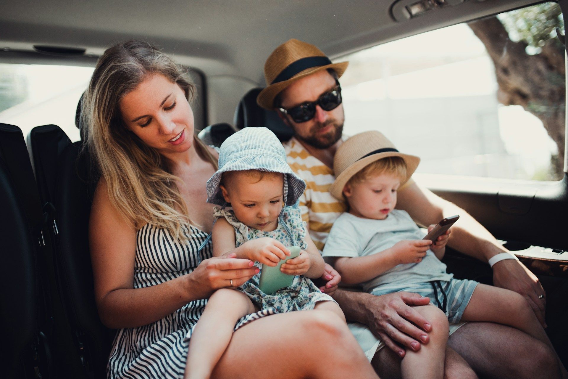 Family sitting together in a car, looking at a phone during a drive