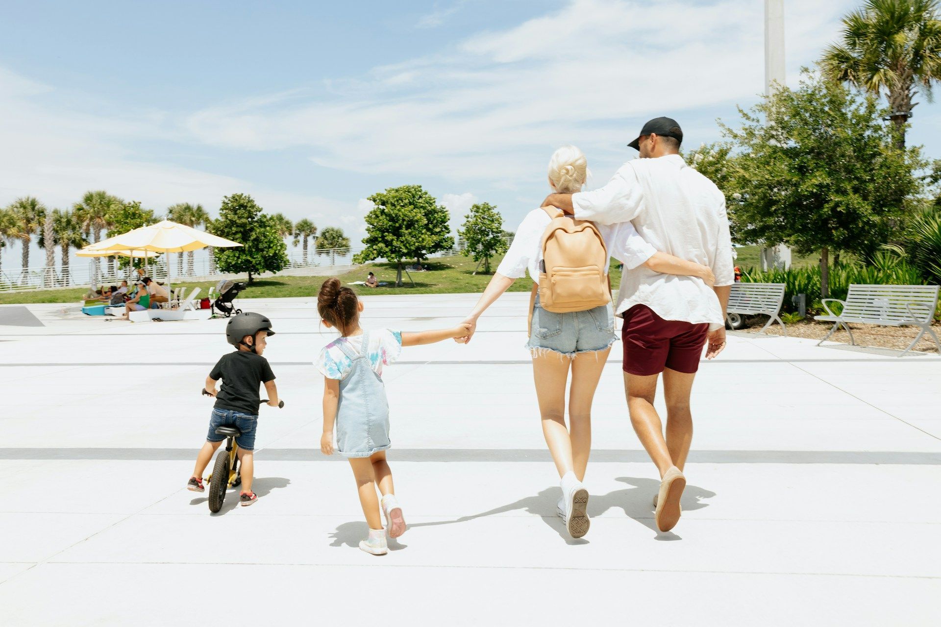 Family walking hand in hand across a sunny plaza near a splash pool