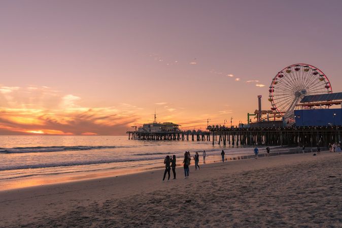 Sunset beach with pier, Ferris wheel, and people walking along the shore