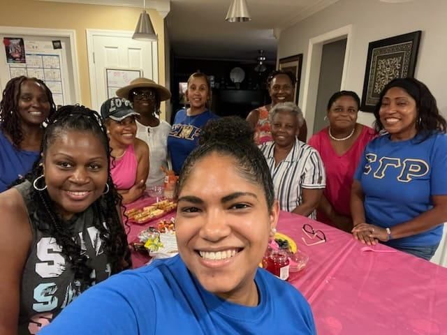 Group of smiling Black women, some wearing blue and pink, at a party with food and drinks.