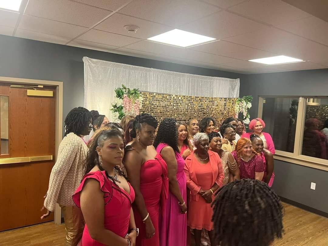 Group of women in pink attire posing for a photo in a decorated room.