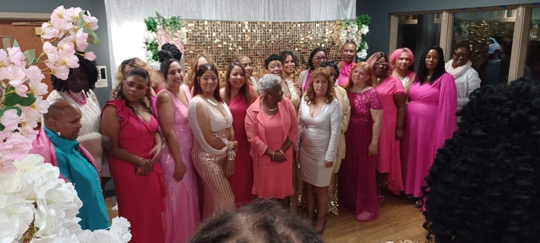 Group of women in pink dresses pose for a photo indoors with floral decorations.