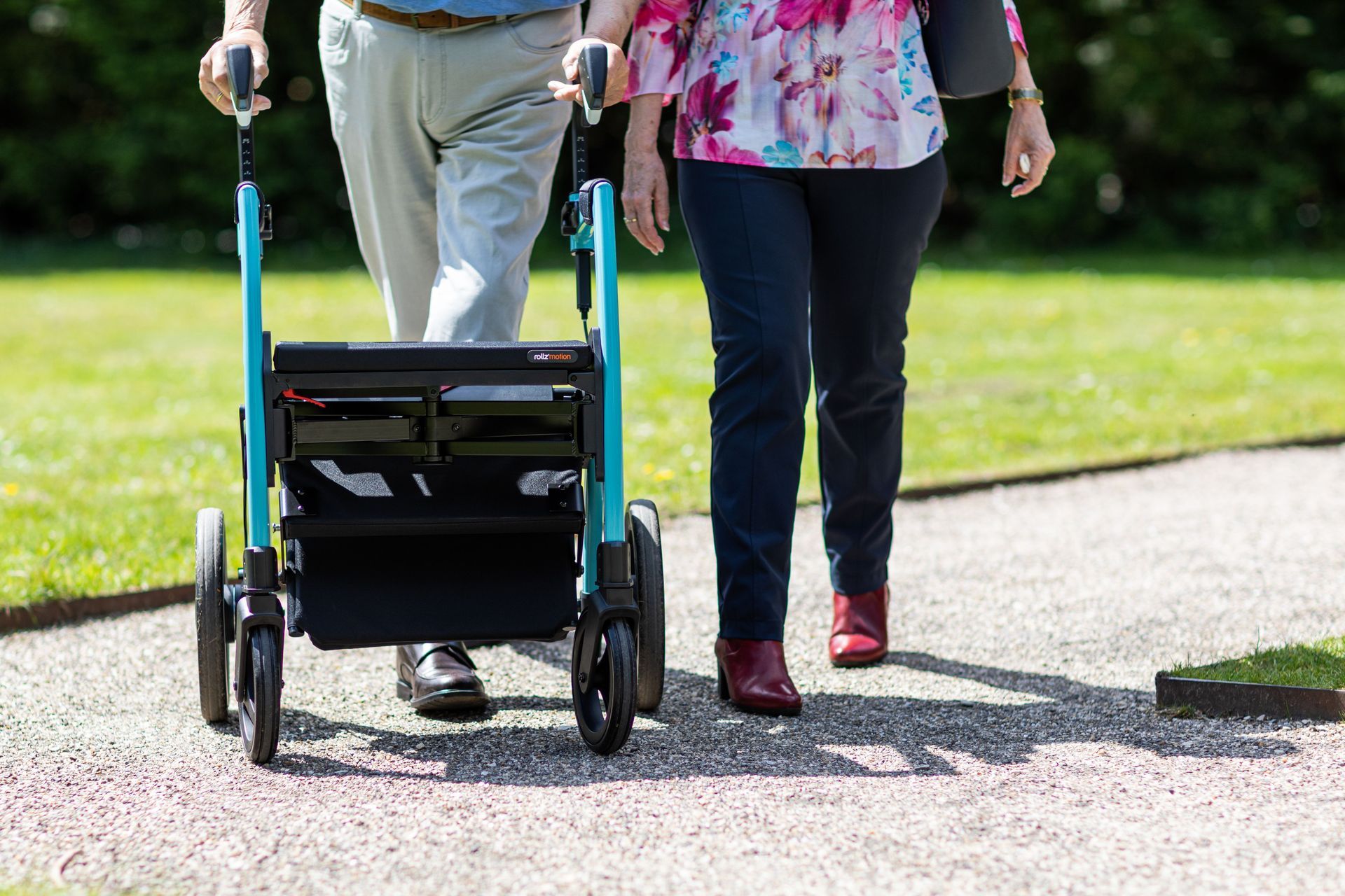 Two people walking on a path, one using a blue rollator walker.