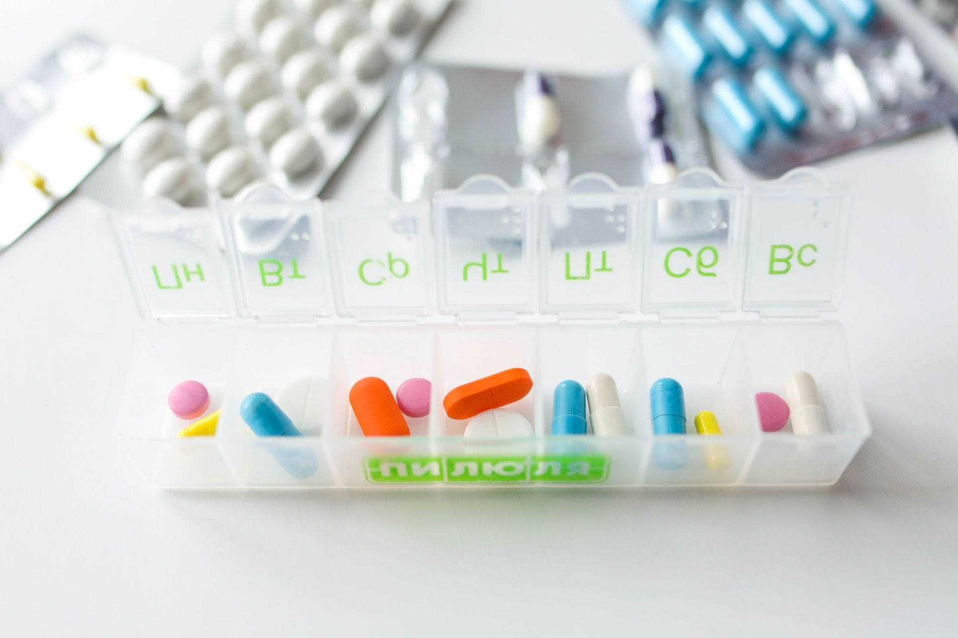 Weekly pill organizer with colorful pills in labeled compartments on a white table