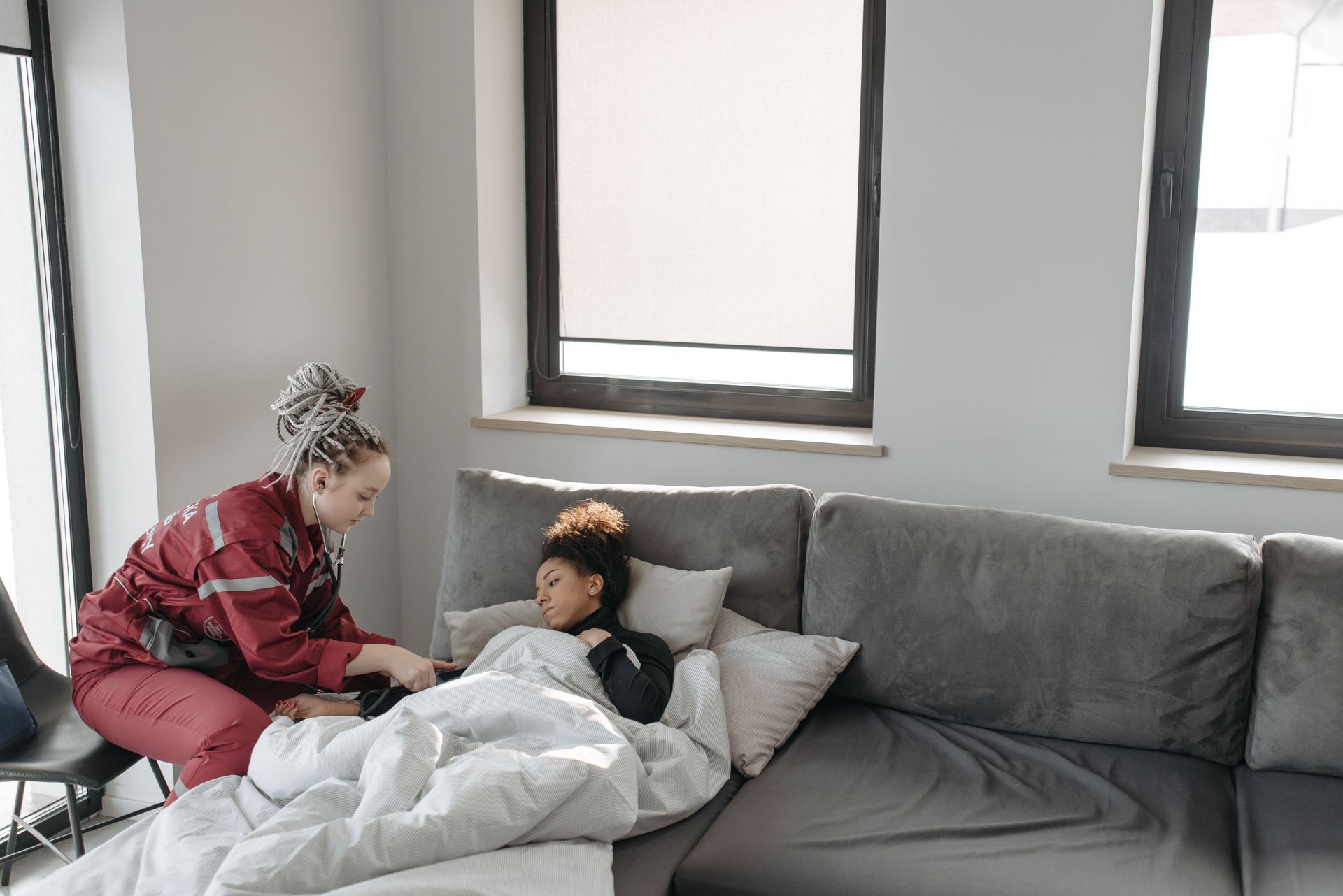 Adult comforting a child under a blanket on a gray couch in a bright living room