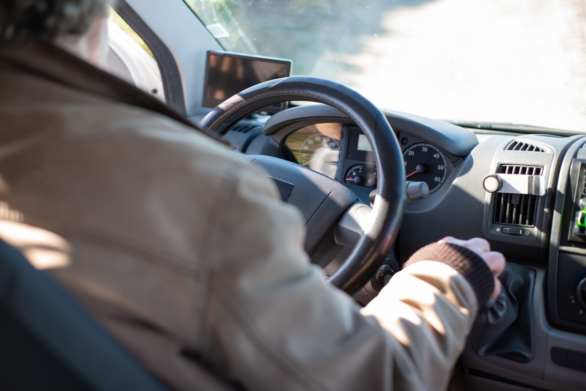 Person driving a car, hand on the steering wheel and other on the gear shift, with a phone mounted on the dashboard