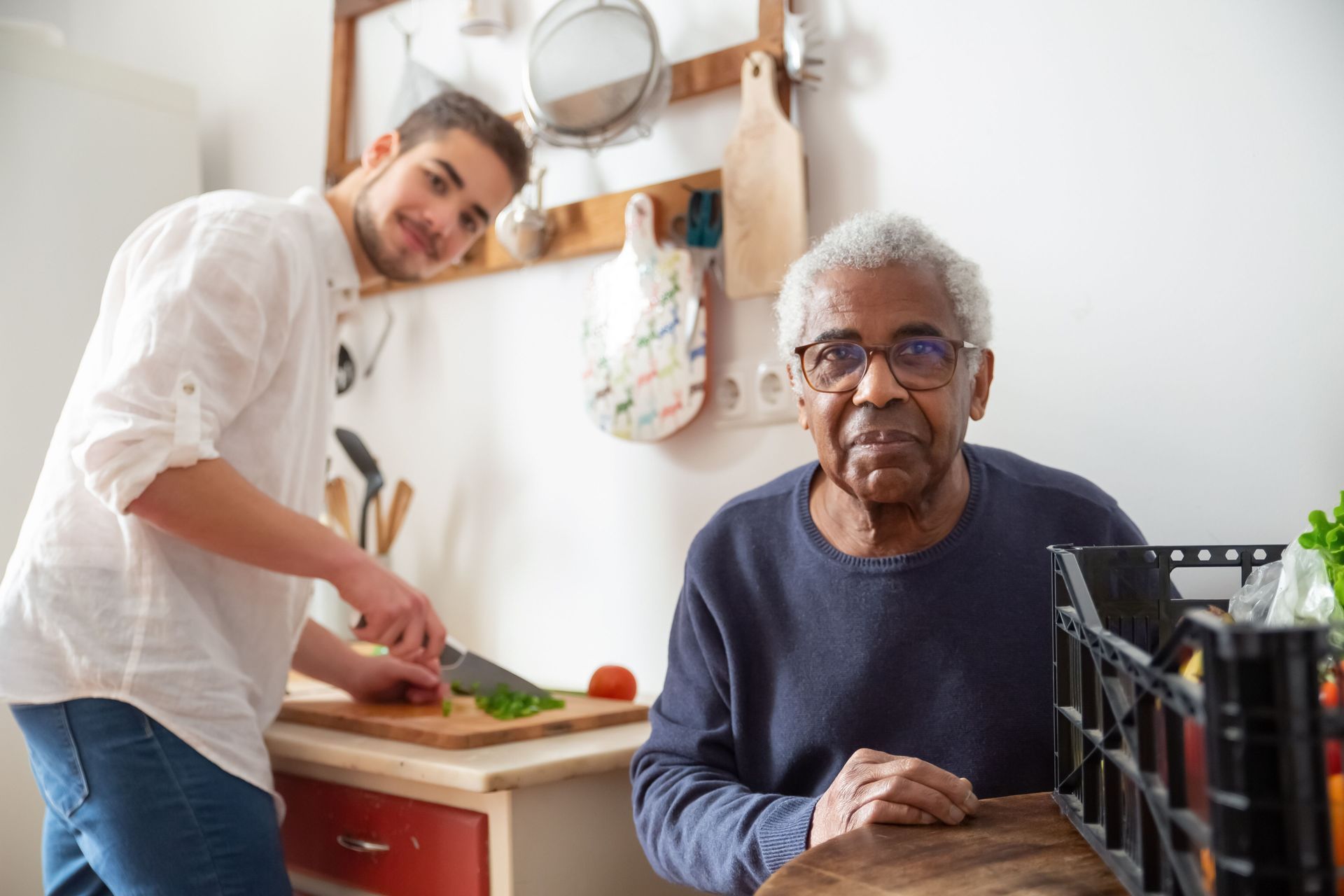 Two people in a kitchen, one chopping vegetables while the other sits at a table.
