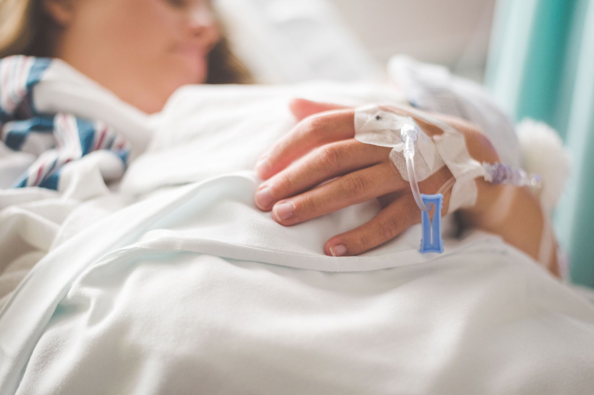 Hospital patient resting in bed with IV line in hand