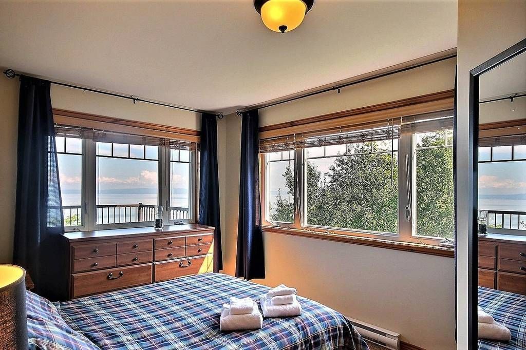 Bedroom with a bed, dresser, windows overlooking a body of water, and dark blue curtains.