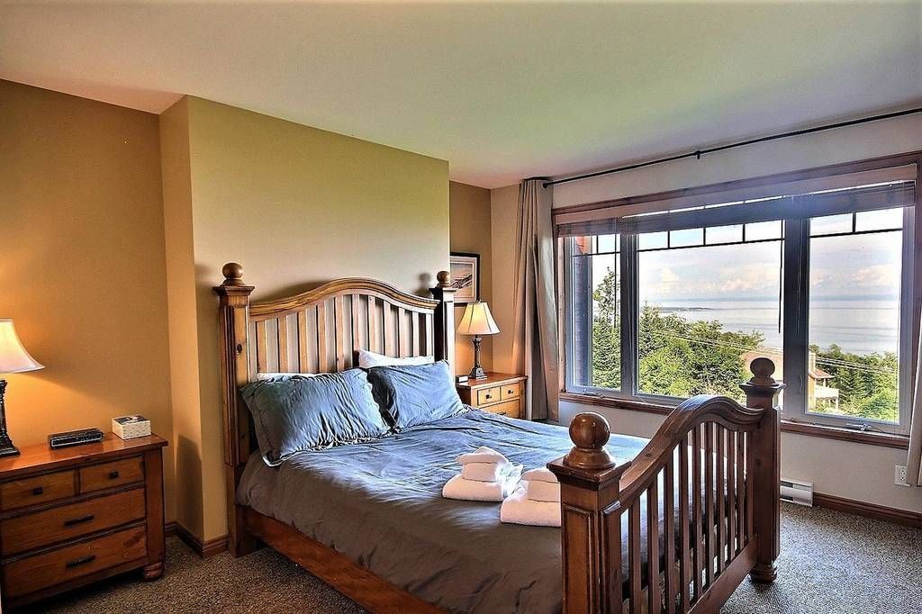 Bedroom with wooden bed frame, view of trees and water through a large window, neutral colors.