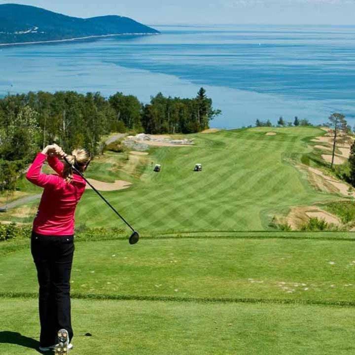 Une femme vêtue de rouge fait tournoyer un club de golf sur un parcours verdoyant surplombant l'océan.