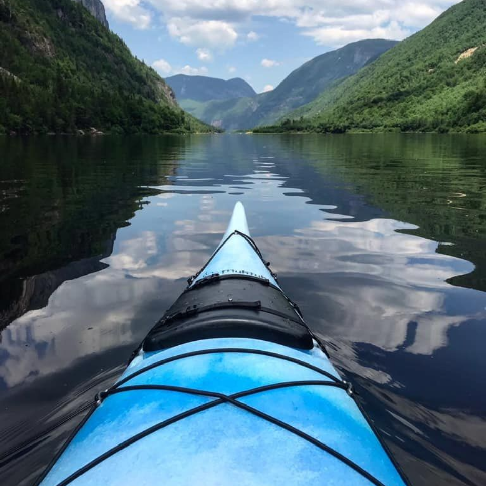Un kayak bleu glisse sur une eau calme, reflétant le ciel et les montagnes.