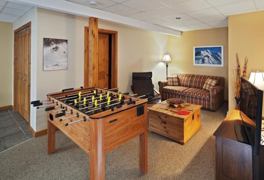 Foosball table and seating area in a finished basement:  tan walls, carpet, wooden accents, and a sofa.
