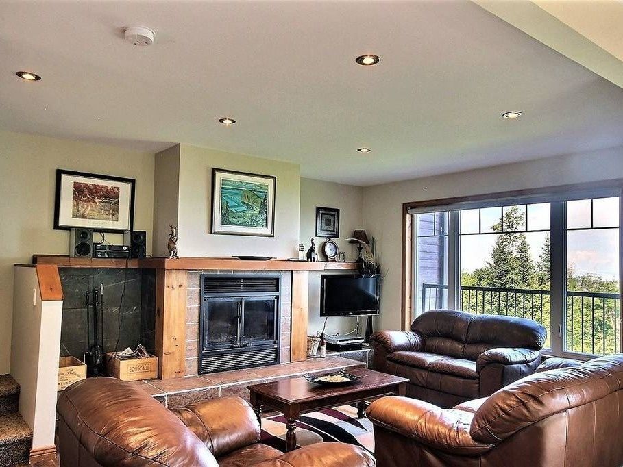 Living room with fireplace, brown leather sofas, large window, and artwork.