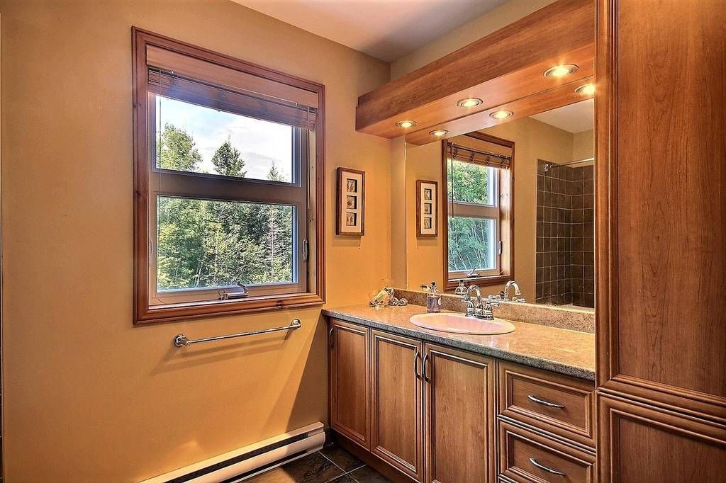 Bathroom with wooden cabinetry, window overlooking trees, and a vanity with a mirror.