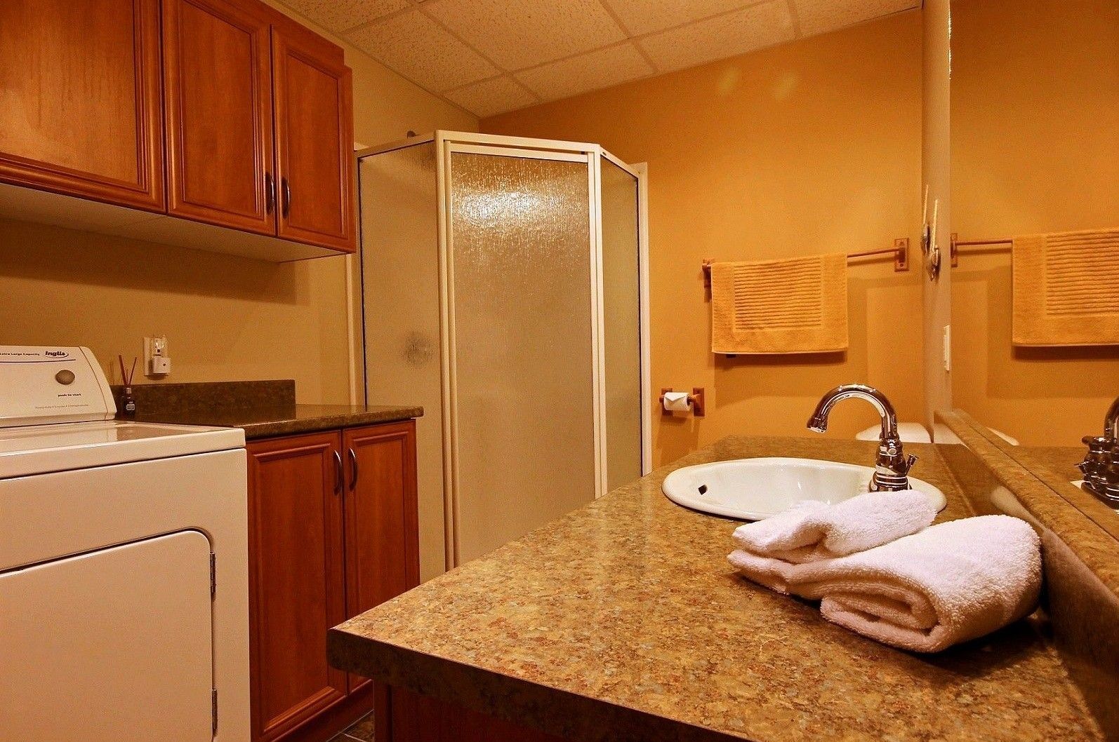 Bathroom with brown cabinets, sink, glass shower, and laundry machine.
