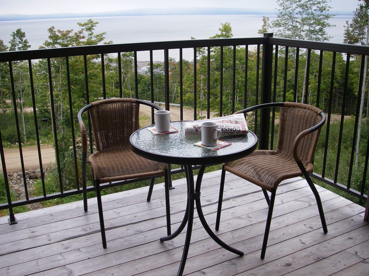 Balcon avec table, deux chaises et boissons donnant sur un lac.
