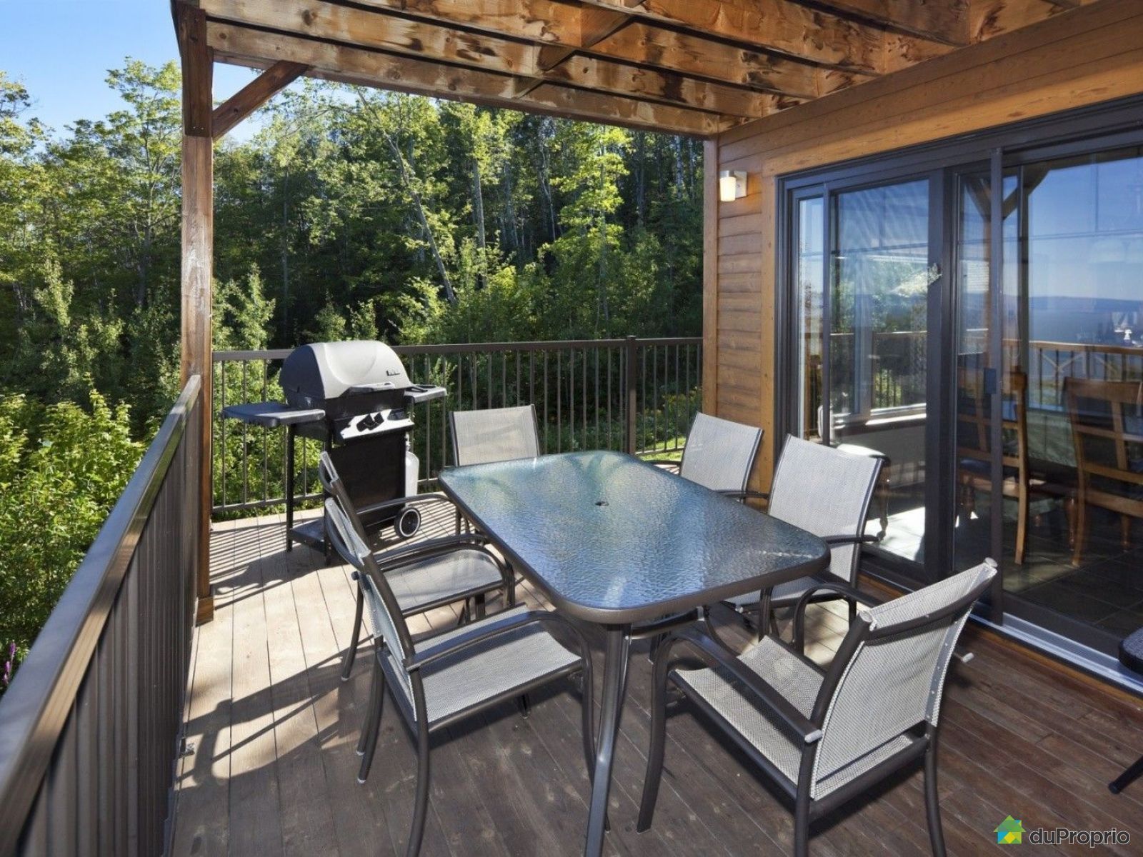 Deck with outdoor dining table, grill, and sliding glass doors, overlooking trees.