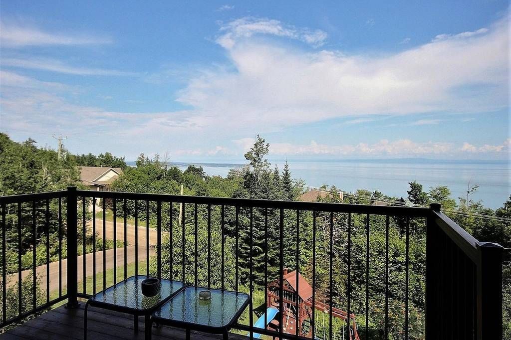 Balcony view overlooking a body of water and distant land, with black railing and two glass-topped tables.