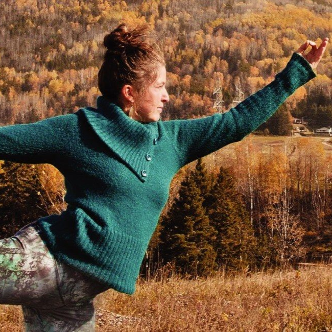 Femme en pull turquoise en équilibre à l'extérieur, bras tendu, paysage d'automne.