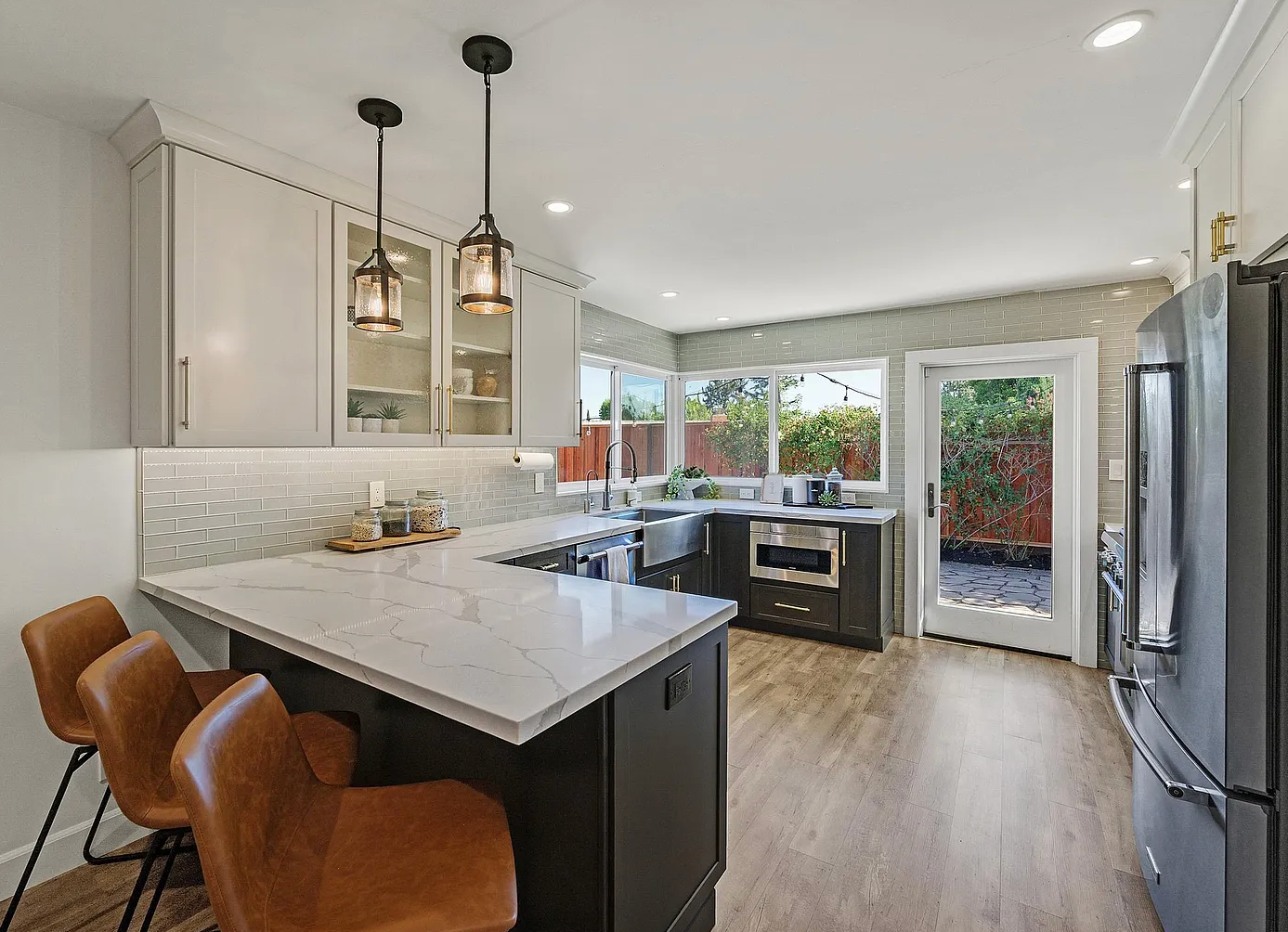 Modern kitchen with bar seating, gray and white cabinets, stainless steel appliances, and a door to the backyard.