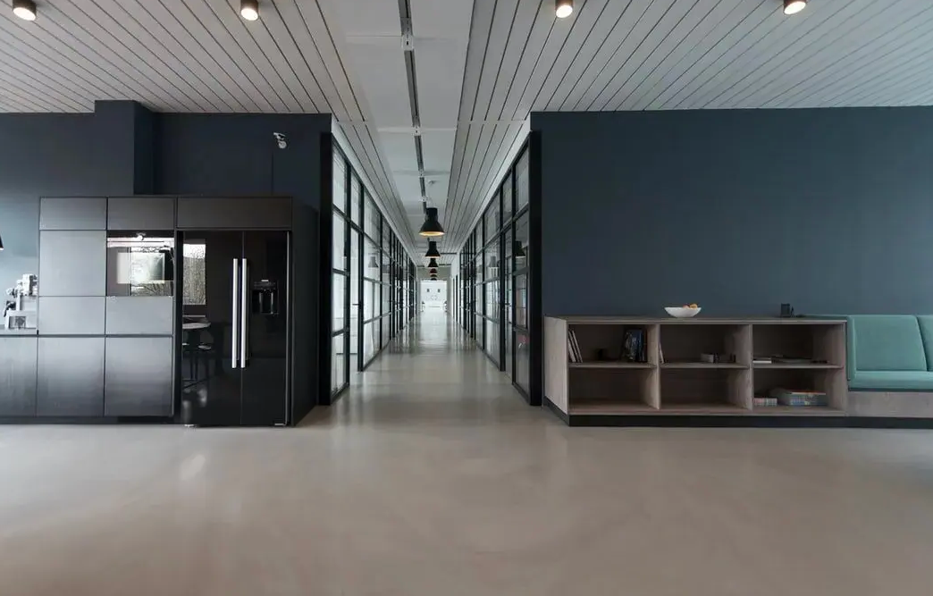 Long office hallway with glass-walled rooms, leading to a light at the end. 